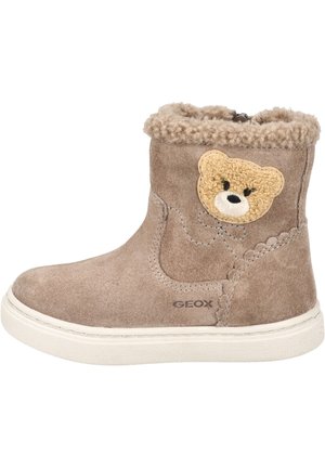 Bottine en suède beige avec garniture en fausse fourrure, appliqué brodé d'un ours et côtés élastiques pour un enfilage facile. Semelle en caoutchouc blanche, accents de couture décoratifs.