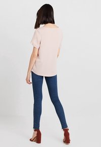 Ljust rosa kortärmad topp i kombination med mörkblå tajta jeans och röda klackar; mjukt tyg med rundad nederkant och subtil söm.