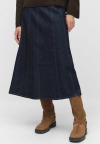Granatowa spódnica dżinsowa z pionowymi szwami, rozkloszowanym fasonem i długością do połowy łydki. Połączona z brązowymi butami na grubej podeszwie z paskami.