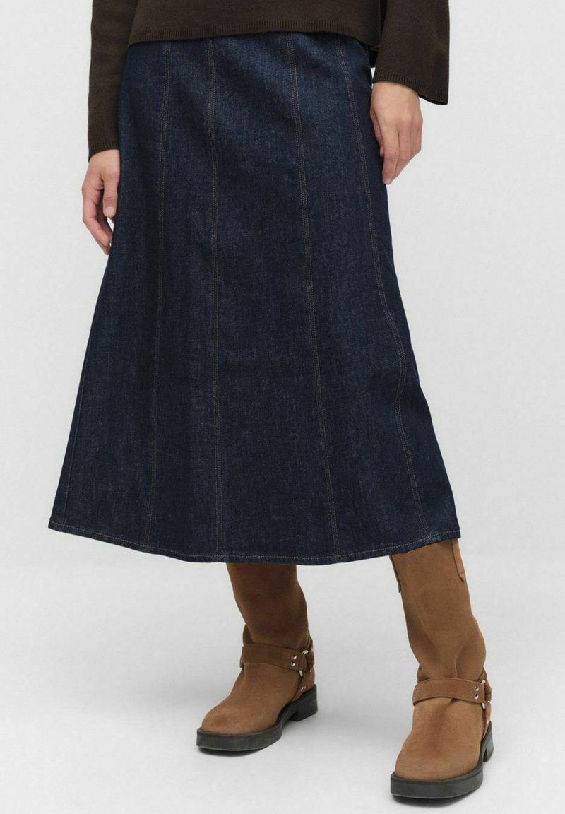 Granatowa spódnica dżinsowa z pionowymi szwami, rozkloszowanym fasonem i długością do połowy łydki. Połączona z brązowymi butami na grubej podeszwie z paskami.