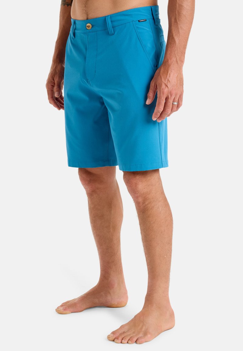Blue shorts made of lightweight fabric, featuring a button closure, flat front, and side pockets. Smooth texture; knee-length design.