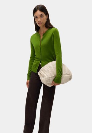 Cardigan verde con scollo rotondo e chiusura a bottoni, abbinato a pantaloni scuri e una grande borsa beige plissettata con una consistenza morbida.