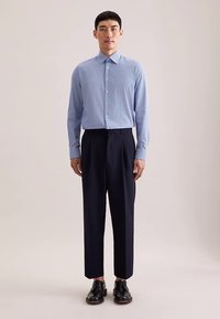 Lichtblauw overhemd met patroon en een kraag, gecombineerd met donkerblauwe geplooide broek en zwarte schoenen. Eenvoudig ontwerp, getailleerde pasvorm en gladde textuur.