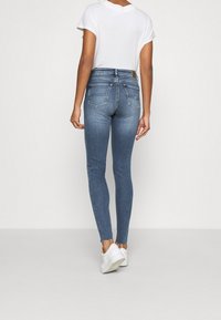 Vaqueros ajustados de denim azul desgastado, con una cinturilla de altura media y bolsillos traseros clásicos. Combinados con una camiseta blanca de cuello redondo y zapatillas blancas.