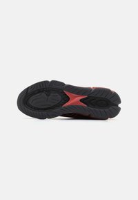 Black rubber shoe sole with prominent traction patterns, featuring red accents and a textured surface. Curved and ergonomic design.