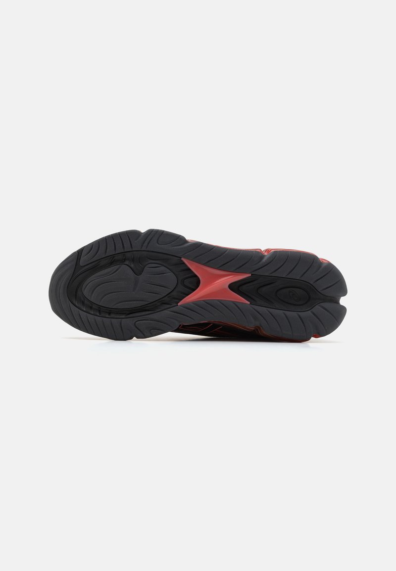 Suela de zapato de goma negra con patrones de tracción prominentes, que presenta acentos rojos y una superficie texturizada. Diseño curvado y ergonómico.