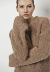 Bruine, fuzzy gebreide trui met een losse, oversized pasvorm en brede mouwen. Heeft een diepe V-hals en een zachte, gestructureerde stof.