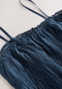 Vestido azul marino con tirantes finos, con tela fruncida, ribete de encaje y superficie texturizada con paneles verticales.