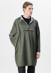 Žalias lengvas gobtuvas su užtrauktuku, pilku pamušalu, kritinėmis petnešomis ir oversize siluetu, pagamintas iš lygaus, vandeniui atsparaus medžiagos.