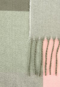 Uldblandet tørklæde med et ternet mønster i dæmpet grøn og lys pink med frynser i kanten, der viser en blød, tekstureret overflade.