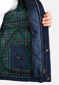 Navy corduroy jacket with quilted blue lining and green plaid interior. Includes a small blue pocket and gold hardware accents.