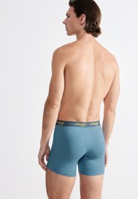 Boxers ajustados para hombre en tejido azul con una textura suave y una cintura amarilla que presenta el nombre de la marca "sloggi."