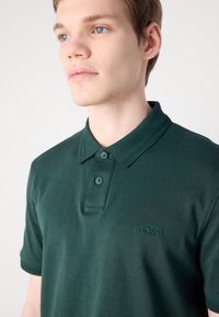 Zelená polokošeľa z bavlny s klasickým golierom, zapínaním na dva gombíky a vyšívaným logom "BOSS" na hrudi.