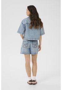 Svetlo modra denim jakna s kratkimi rokavi in nekoliko skrajšano zasnovo, v kombinaciji z ujemajočimi se hlačami do pasu, ki imajo zadnje žepe.