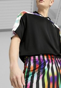 Sort sports skjorte med regnbue-mønstrede ærmer, parret med farverige stribede shorts med lodrette sorte striber og livlige nuancer.