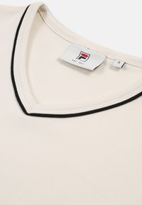 Crème-kleurige V-hals T-shirt met zwarte afwerking. Heeft een merklabel in de hals. Gemaakt van zachte stof, maat S.