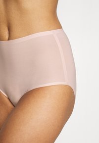 High-waisted, sheer pink underwear with a smooth texture and seamless edges. Soft fabric offers a minimalistic design with no visible hardware.