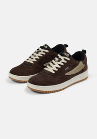 Bruna mockaskor med krämfärgade snören och sula av gummirubber. Har texturerade detaljer och en logotyp på den platta tungan och sidan.