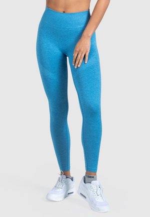 Leggings blu a vita alta in un tessuto testurizzato e stretchy, abbinati a scarpe da ginnastica bianche, che mostrano un design aderente.