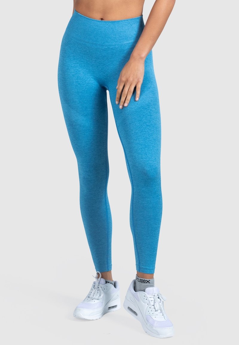 Leggings blu a vita alta in un tessuto testurizzato e stretchy, abbinati a scarpe da ginnastica bianche, che mostrano un design aderente.