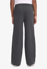 Φαρδύ παντελόνι σε σκούρο γκρι, με λείο, ελαστικό ύφασμα και ελαστική μέση. Το τελείωμα φτάνει λίγο πάνω από τα παπούτσια.