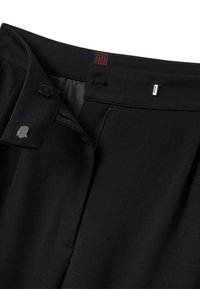 Pantalones negros de corte ajustado con una tela suave, cremallera en la bragueta y una cintura plana con dos botones y un detalle plateado.