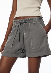 Pantalones cortos de algodón gris con cintura elástica y cordón, que cuentan con dos bolsillos laterales y dobladillos enrollados. Textura suave y diseño informal.