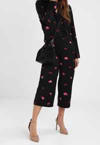 Černý outfit s barevným potiskem rtů. Volný top a zkrácené kalhoty skombinované s černou kabelkou a neutrálními vysokými podpatky.