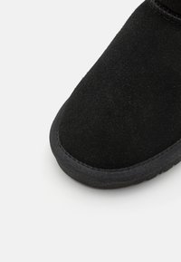 Botín de ante negro con punta redonda, textura suave y suela de goma. La costura es tonal, fusionándose a la perfección con el material superior.