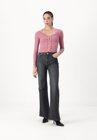 Rožnata rebrasta dolgosleeve majica z čipkastim robom in gumbi, v kombinaciji z visokim temnim flare jeansom in črnimi škornji s peto.