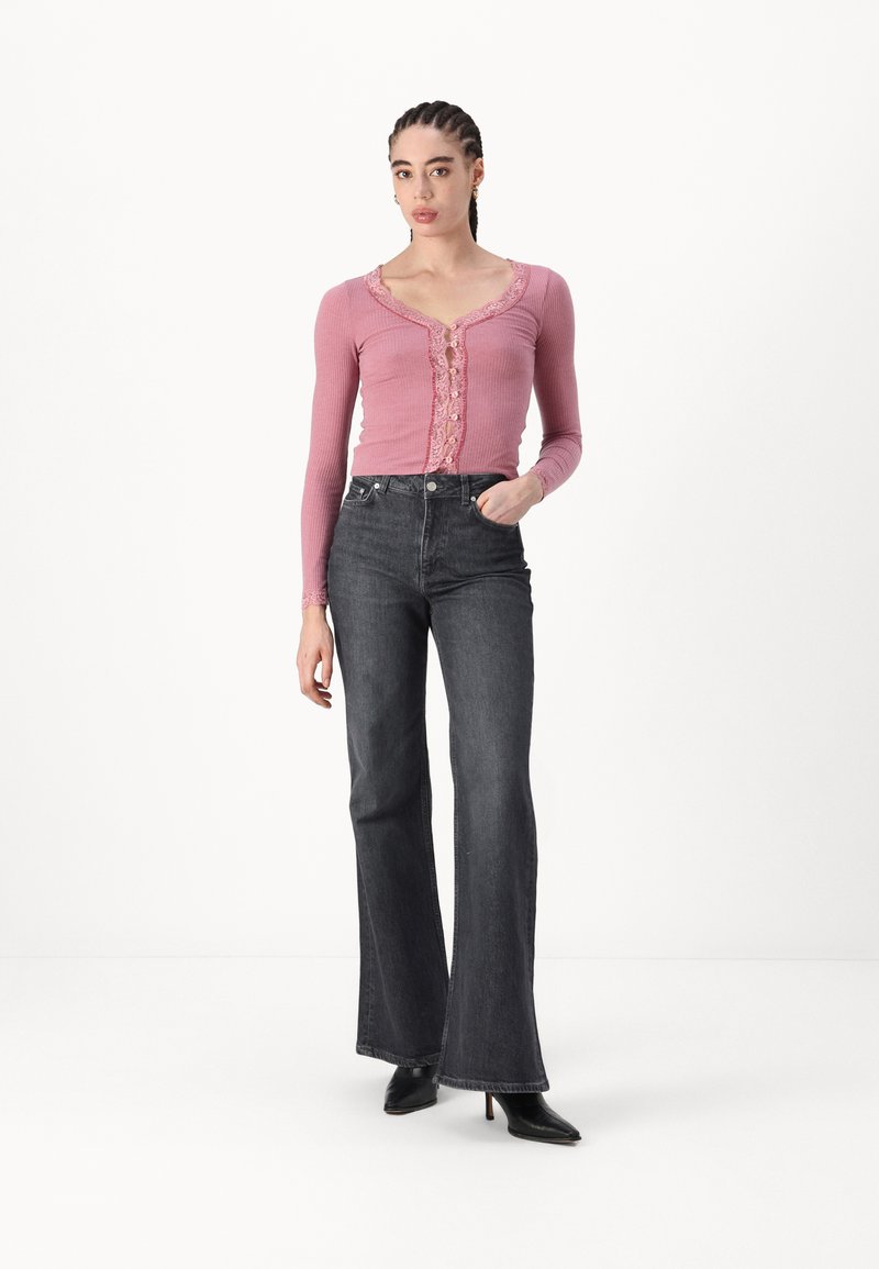 Haut rose à manches longues côtelé avec bord en dentelle et boutons, associé à un jean flare noir taille haute et des bottes noires à talons.