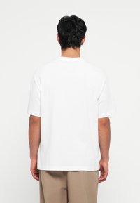 Camiseta blanca de manga corta, hecha de algodón, con cuello redondo clásico y un ajuste relajado. Textura suave sin patrones o herrajes visibles.