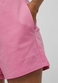 Rosa bomullsshorts med avslappnad passform, med sidofickor och subtil broderad text nära fållen. Mjuk textur med avslappnad design.