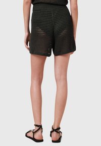Zwarte mesh shorts met een gestructureerd, open gebreid ontwerp, voorzien van een brede elastische tailleband en opgerolde manchetten. Opvallend door de ademendheid.