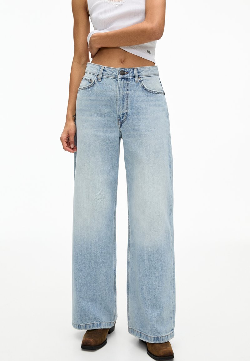 Jean large bleu clair en denim, avec une taille haute, des coutures visibles et un design à cinq poches. Le tissu a une texture lisse.