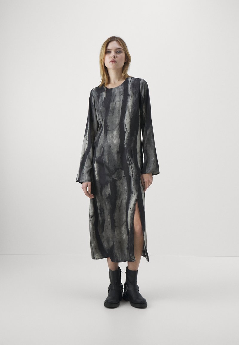 Rochie lungă neagră cu modele abstracte gri, având mâneci lungi, fente laterale și o textură netedă. Asortată cu botine negre până la gleznă.