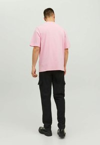 T-shirt en coton rose à manches courtes et coupe droite, associé à un pantalon cargo noir avec poches latérales et texture lisse.