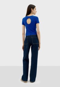 Haut bleu à manches courtes côtelé avec un détail en forme d'œillet dans le dos, associé à un jean en denim noir taille haute et des chaussures beiges en peluche.