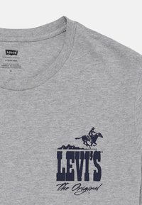 Camiseta de algodón gris con cuello redondo, con un gráfico en azul marino de un jinete a caballo y el texto "LEVI'S the Original."