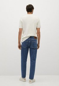 Camisa blanca de manga corta, jeans de denim azul, corte ajustado, bolsillos traseros visibles, etiqueta de cuero marrón claro en la cinturilla, combinada con zapatillas ligeras.