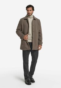 Brun ullblandning kappa med en krage design, knappar och sidofickor. Halvklart med en ljus tröja, mörka jeans och svarta skor.