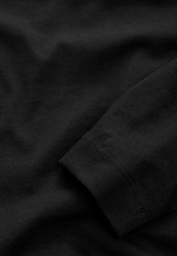 Gros plan d'un tissu noir montrant une manche pliée avec des coutures visibles et une texture lisse.