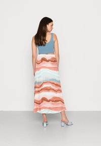 Vestido maxi com um topo canelado azul claro e uma saia fluida com padrões ondulados em rosa, castanho e azul. Usado com sandálias de salto azul claro.