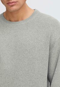 Grauer Strickpullover mit Rundhalsausschnitt und strukturierter Oberfläche. Das Gewebe ist fein und zeigt ein einheitliches Muster über die gesamte Fläche.
