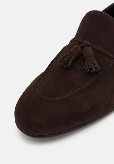 Rudos zomšos loafers'ai su apvaliu pirštu ir dekoratyvinėmis kutais priekyje. Kontrastinga siuvinėjimo detalė papildo dizainą. Lygus padas.