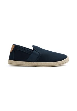 Zapato sin cordones de lona azul marino con suela beige texturizada y lengüeta marrón en el talón, mostrado en perfil lateral sobre fondo blanco.