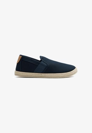 Zapato sin cordones de lona azul marino con suela beige texturizada y lengüeta marrón en el talón, mostrado en perfil lateral sobre fondo blanco.