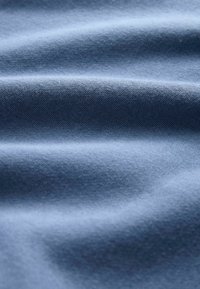 Zacht, gestructureerd blauw textiel met een gladde afwerking, voorzien van zachte golven en plooien die de diepte en visuele aantrekkingskracht versterken.