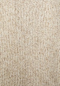 Pull en tricot épais de couleur crème et beige. Présente un point texturé avec un mélange de fils, créant un aspect doux et superposé.