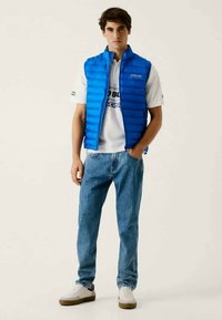 Modra podložena jakna čez belo srajco z modrim napisom, v kombinaciji z svetlimi kavbojkami in belimi supergami. Preprosta zasnova, sproščen kroj.